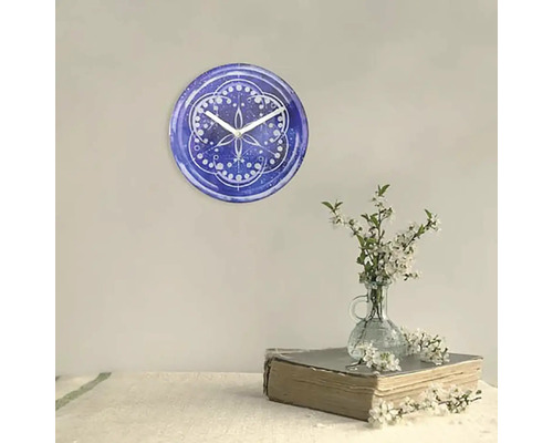 Nástenné hodiny s modrým vzorom a bielymi ručičkami vedľa vázy s kvetmi