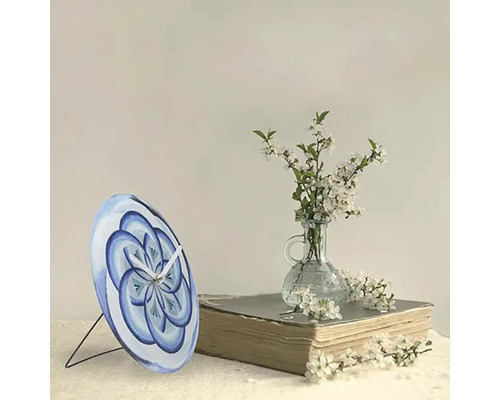 Stolové hodiny s modrým kvetinovým vzorom na knihe vedľa vázy s kvetmi