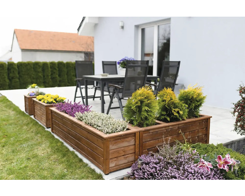 Drevené kvetináče s rôznymi rastlinami v záhrade a terasový nábytok v pozadí.