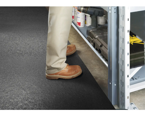 Muž stojí na gumovej podložke pred úložným regálom s náradím a príslušenstvom.