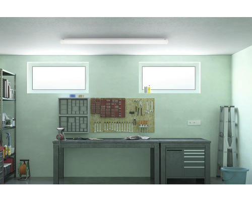 Dielňa s pracovným stolom, stenou na náradie a policami pod stropným svietidlom.