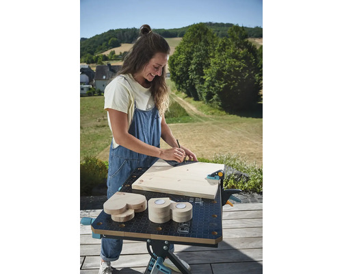 Žena pracuje vonku na pracovnom stole s drevom, uholníkom a ceruzkou.