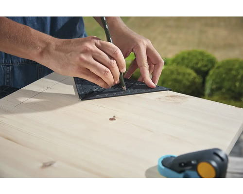 Osoba kreslí čiaru pomocou uholníka a ceruzky na drevenú dosku.