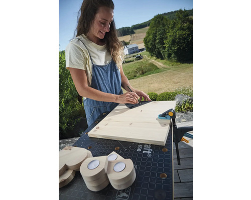 Žena rysová čiaru na drevenej doske pomocou uholníka na ponku so skrutkovacou svorkou a drevenými srdiečkami