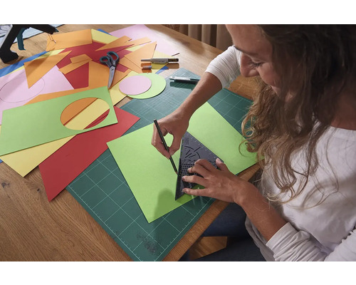 Žena kreslí zelenú papierovú šablónu pomocou trojuholníka, podložky a ceruzky.