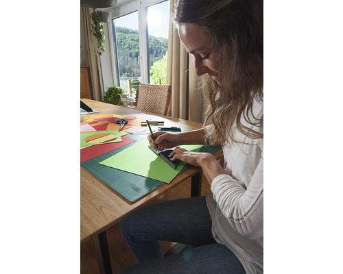 Žena pracuje s papierom, pravítkom a ceruzkou pri stole.