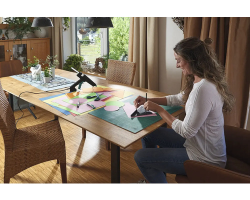 Žena vyrába na stole s tavnou pištoľou, papierom, nožnicami a podložkou na rezanie