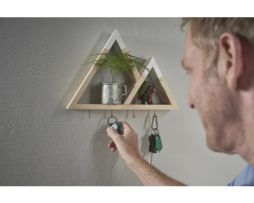 Dekoratívna nástenná polica v tvare hory s háčikmi na kľúče a osobou, ktorá zavesuje zväzok kľúčov