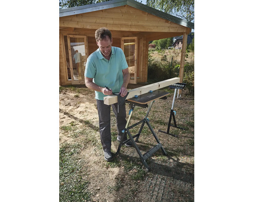 Muž kreslí čiaru na drevenej doske pomocou uholníka a ceruzky na pracovnom stole v záhrade.