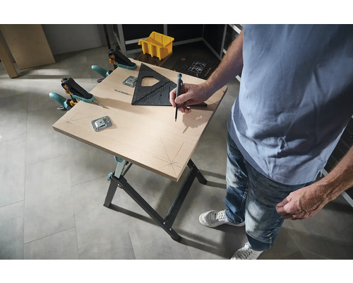 Pracovný stôl s osobou, ktorá ceruzkou kreslí čiary na drevenú dosku, s uholníkom a svorkami na upevnenie