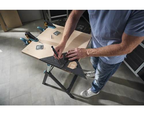 Osoba kreslí uholníkom a ceruzkou na drevený stôl, ktorý je upevnený svorkami.