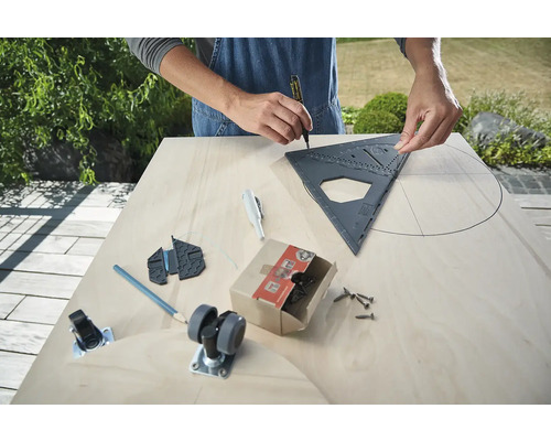 Muž kreslí kruh pomocou uhlomera na drevenej doske, vrátane koliesok, skrutiek a nástrojov