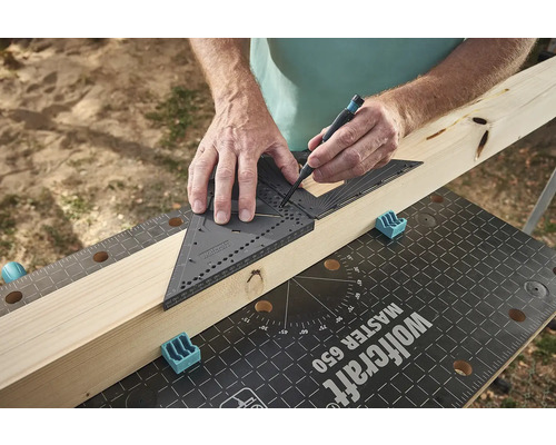 Muž používa tesársky uholník a ceruzku na označenie kusu dreva na pracovnom stole.