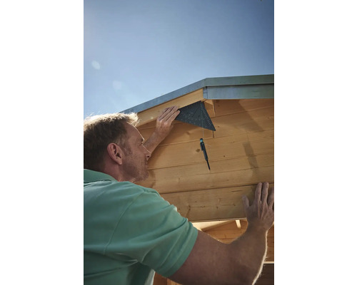 Muž montuje drevený dom s uhlomerom.