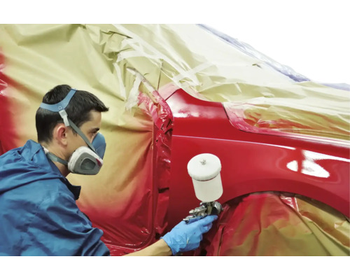 Muž strieka auto farbou pomocou striekacej pištole. Auto je zakryté fóliou.