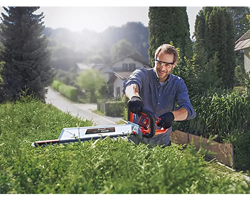 Muž strihá živý plot nožnicami na živý plot vonku.