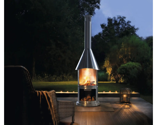 Nerezový terasový krb s drevom na drevenej terase so záhradou v pozadí