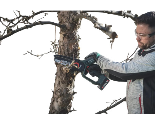 Muž s ochrannými okuliarmi prerezáva strom pomocou akumulátorovej reťazovej píly Metabo.