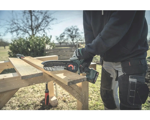 Osoba reže drevo pomocou akumulátorovej reťazovej píly Metabo na drevenom pracovnom stole.