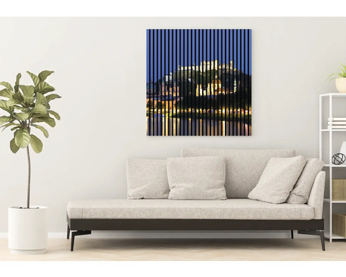 Dekoratívne nástenné umenie s motívom mestskej scenérie za zvislými líniami nad pohovkou v obývacej izbe.