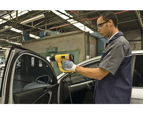 Muž používa teplovzdušnú pištoľ DeWALT na úpravu okna automobilu.