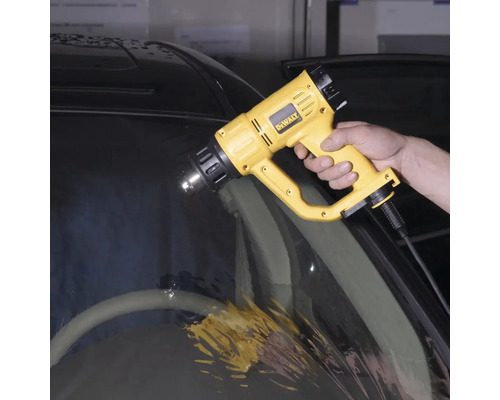 Osoba používa teplovzdušnú pištoľ DeWalt na autosklo.