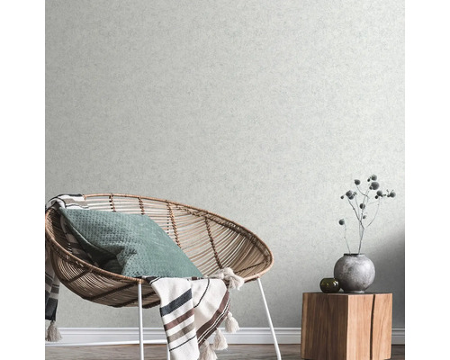 Obývacia izba s ratanovým kreslom, vankúšom, dekou a dreveným odkladacím stolíkom s dekoráciou pred štruktúrovanou tapetou