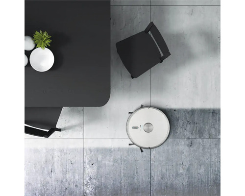 Scéna s robotickým vysávačom pod stolom a stoličkou na dlažbe