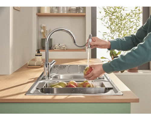 Kuchynský drez s vodovodnou batériou a osobou umývajúcou ovocie