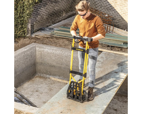Osoba používa schodiskový vozík Stanley na prepravu stavebného materiálu na stavenisku.
