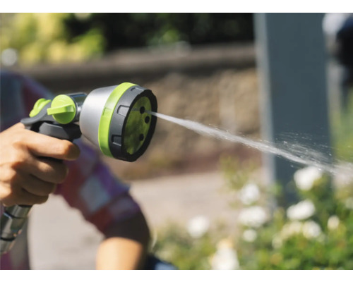 Ruka drží záhradnú striekaciu pištoľ, z ktorej vyteká voda.