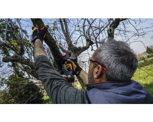 Muž reže konáre stromov akumulátorovou prerezávacou pílou.