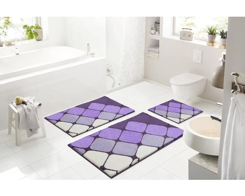 Moderná kúpeľňa s trojdielnou, fialovo-sivou súpravou kúpeľňových koberčekov s geometrickým vzorom pred vaňou, umývadlom a toaletou