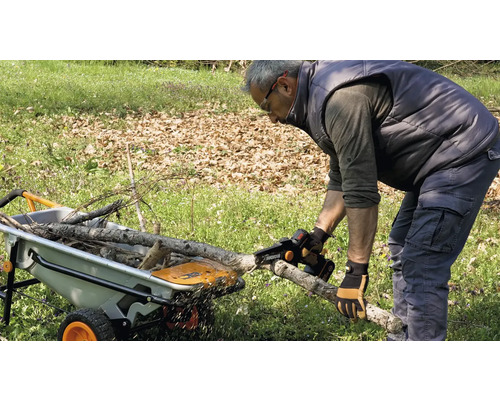 Muž pília vetvu akumulátorovou pílou pred kolieskom.
