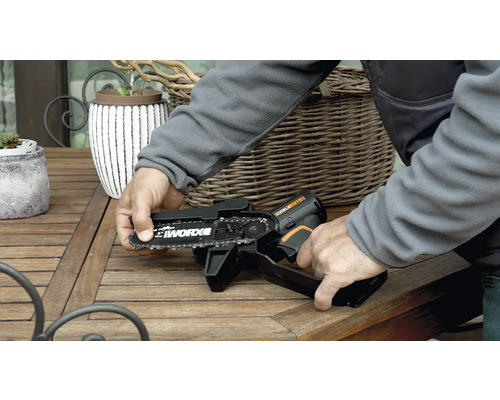 Osoba obsluhuje akumulátorovú reťazovú pílu značky Worx na drevenom stole