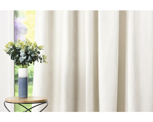 Dekoračná látka so vzorom a stôl s kvetinovou vázou pred oknom