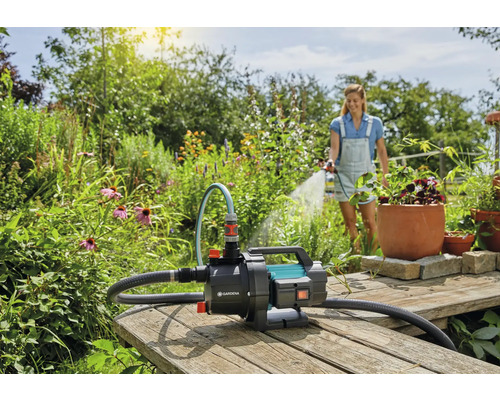 Záhradná scéna so ženou zalievajúcou rastliny záhradným čerpadlom Gardena