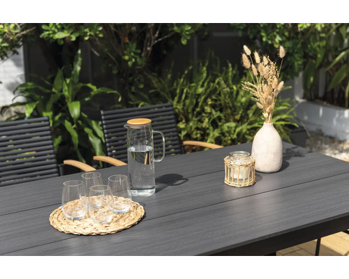 Záhradná scéna so stolom, stoličkami, pohármi, karafou na vodu, sviečkou a dekoráciou.