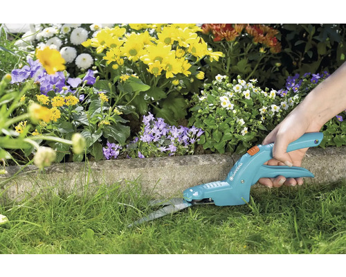 Osoba strihá okraje trávnika záhradnými nožnicami na trávu.