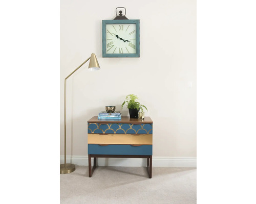 Dekoratívna scéna s nočným stolíkom s tromi zásuvkami, stojacou lampou a nástennými hodinami.