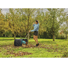 Žena hrable jesenné lístie do vreca na lístie v záhrade