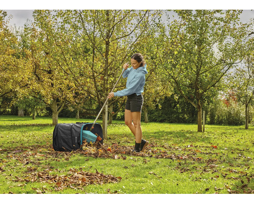 Žena hrable jesenné lístie do vreca na lístie v záhrade
