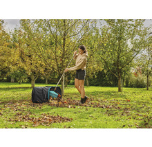 Žena hrabe lístie hrabľami do záhradného vreca v záhrade.