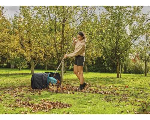Žena hrabe lístie hrabľami do záhradného vreca v záhrade.