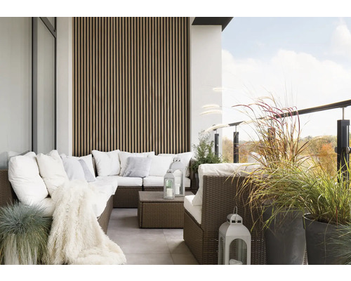 Balkón s ratanovým posedením, vankúše, deka, lampáše a kvetináče.