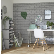 Pracovňa so stolom, stoličkou, policami a dekoratívnymi predmetmi pred sivou tehlovou stenou