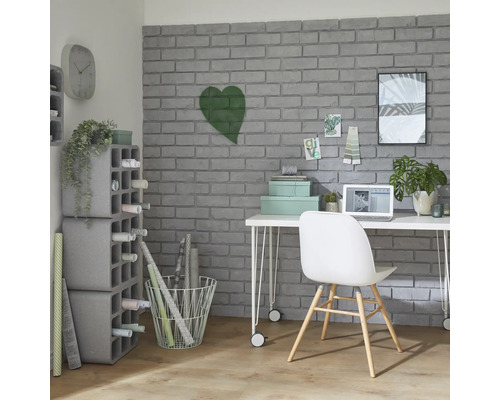 Pracovňa so stolom, stoličkou, policami a dekoratívnymi predmetmi pred sivou tehlovou stenou