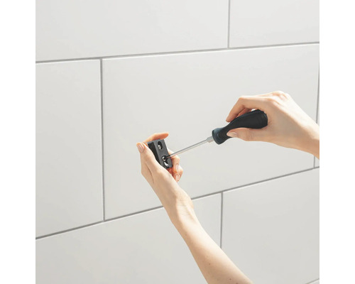 Osoba pripevňuje držiak k stene s obkladmi pomocou skrutkovača.