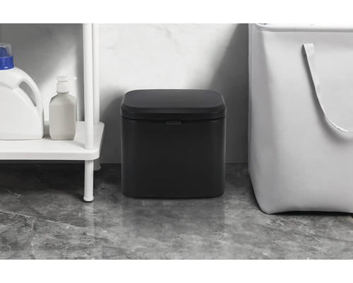 Čierny pedálový kôš v kúpeľni vedľa regálu a koša na bielizeň.