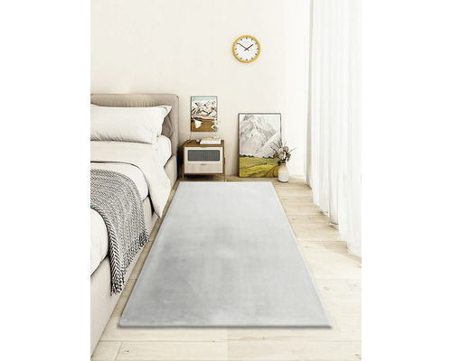 Spálňa s posteľou, nočným stolíkom a sivým kobercom na drevenej podlahe.